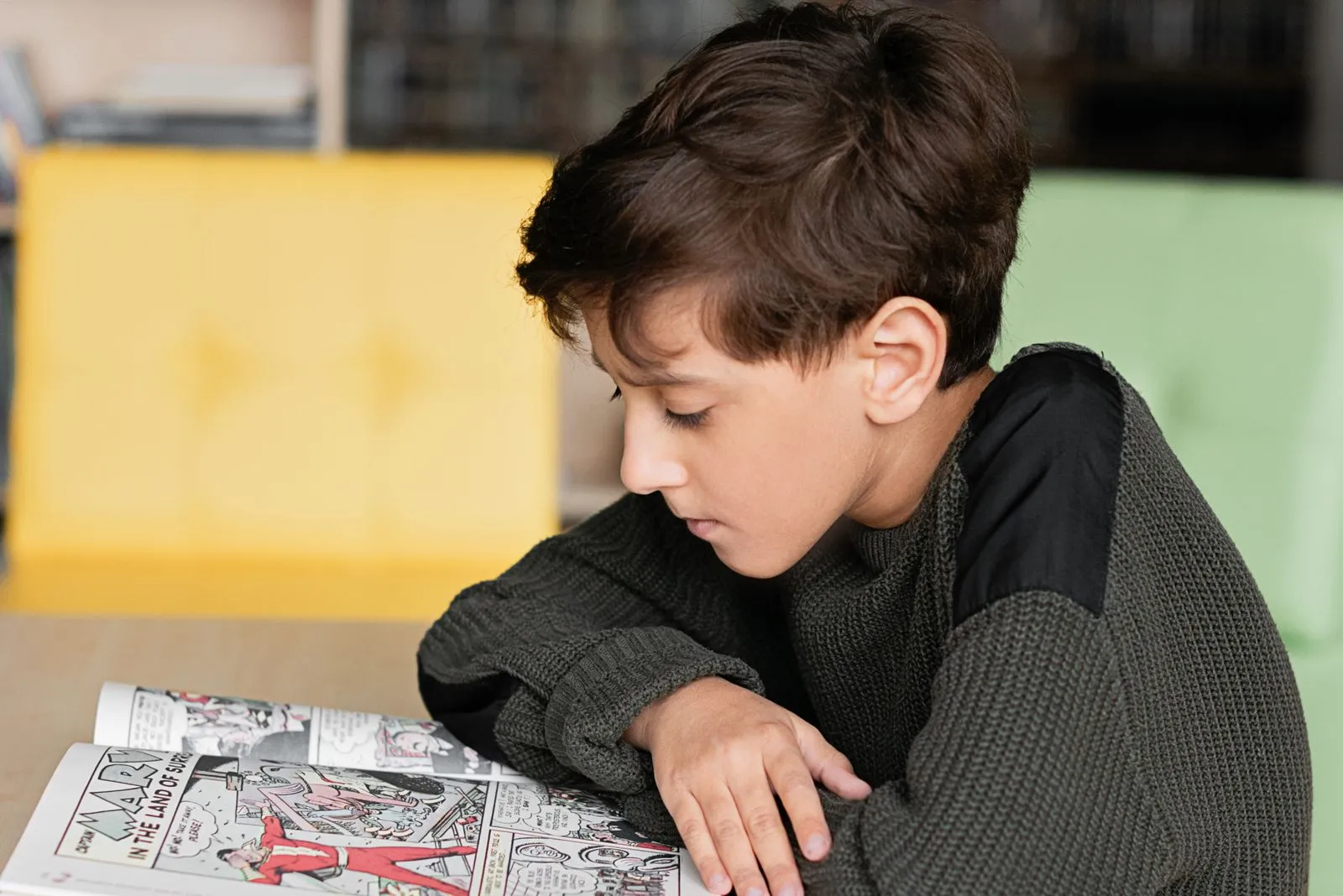A young boy deeply focused on reading a comic book in a cozy indoor setting.